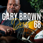 Gary Brown poses confidently with a trophy and football gear, showcasing his achievements and dreams.