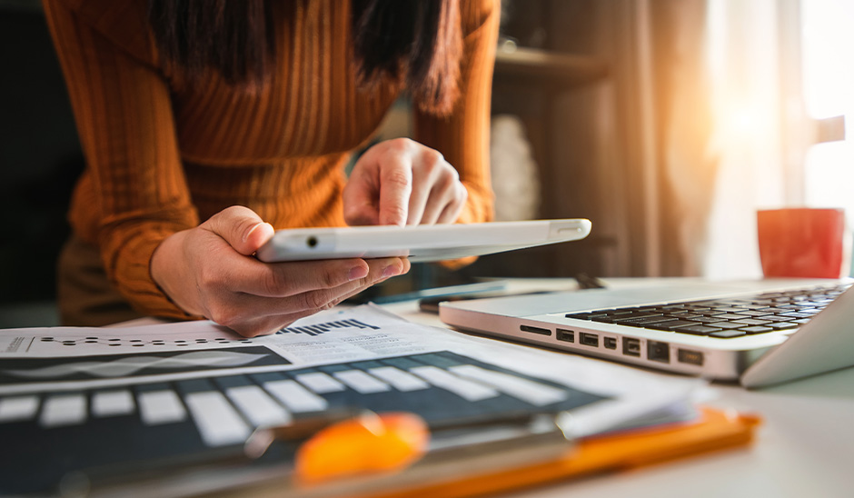 A woman using a tablet while analyzing marketing graphs at a desk