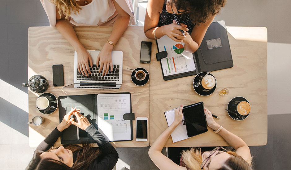 Overhead view of four people collaborating at a table with laptops and coffee.