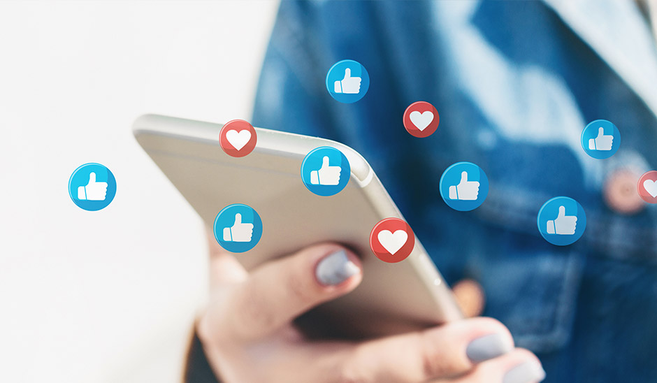 A person holding a smartphone with floating social media reaction icons like thumbs up and hearts.