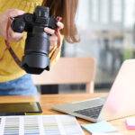 A person holding a camera over a workspace with a laptop and color swatches.