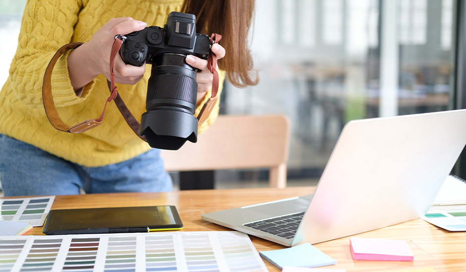 A person holding a camera over a workspace with a laptop and color swatches.
