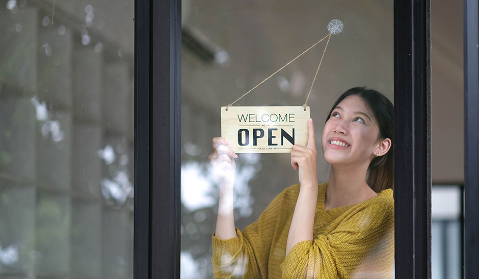 Woman smiling while hanging an 'OPEN' sign at a shop window.