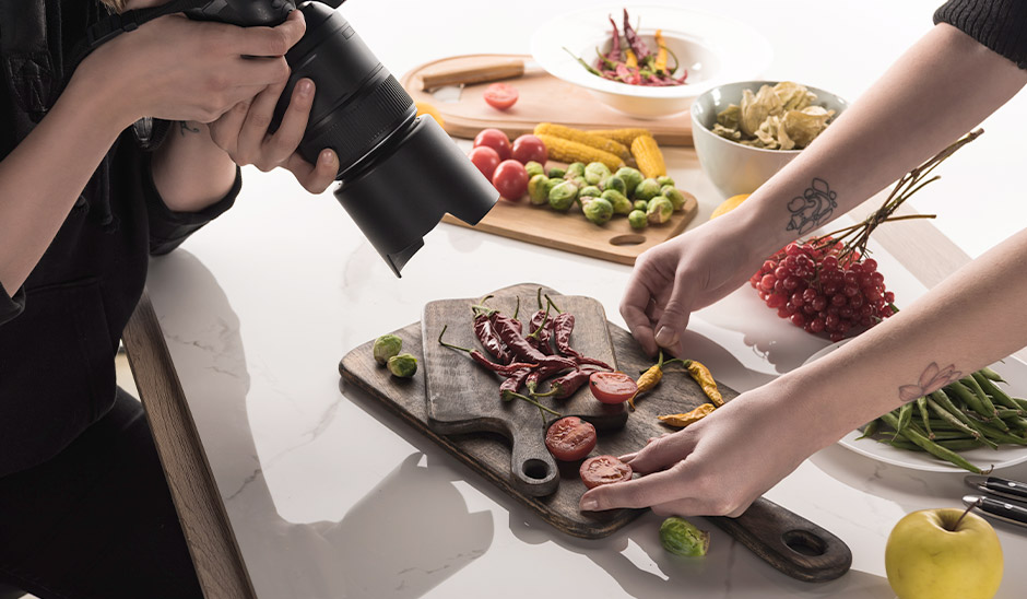 A photographer captures vibrant vegetables and herbs on a wooden cutting board.