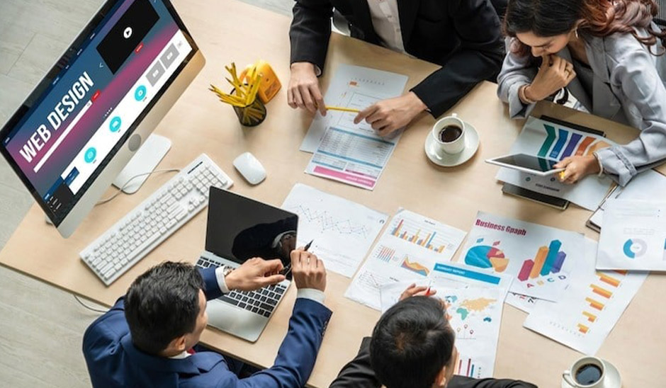 A group of professionals collaborating on web design and marketing strategies around a table with laptops and charts.