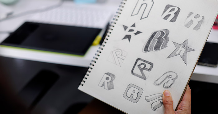 Sketchbook displaying various logo designs and letter styles in pencil.