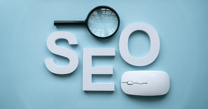 White letters spelling SEO with a magnifying glass and computer mouse on a blue background.