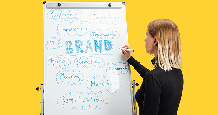A woman writing on a whiteboard covered with brand strategy keywords such as 'Innovation', 'SEO', and 'Marketing'.