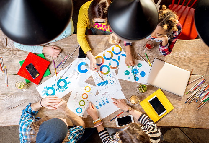 Group of diverse people collaborating over charts and graphs on a wooden table in a well-lit workspace.