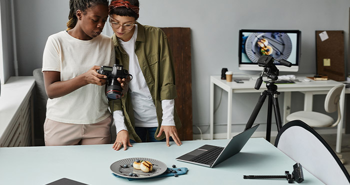 Two women reviewing photos of a dessert in a bright workspace.