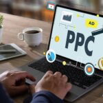 A person typing on a laptop displaying PPC advertising graphics, with a coffee cup nearby.