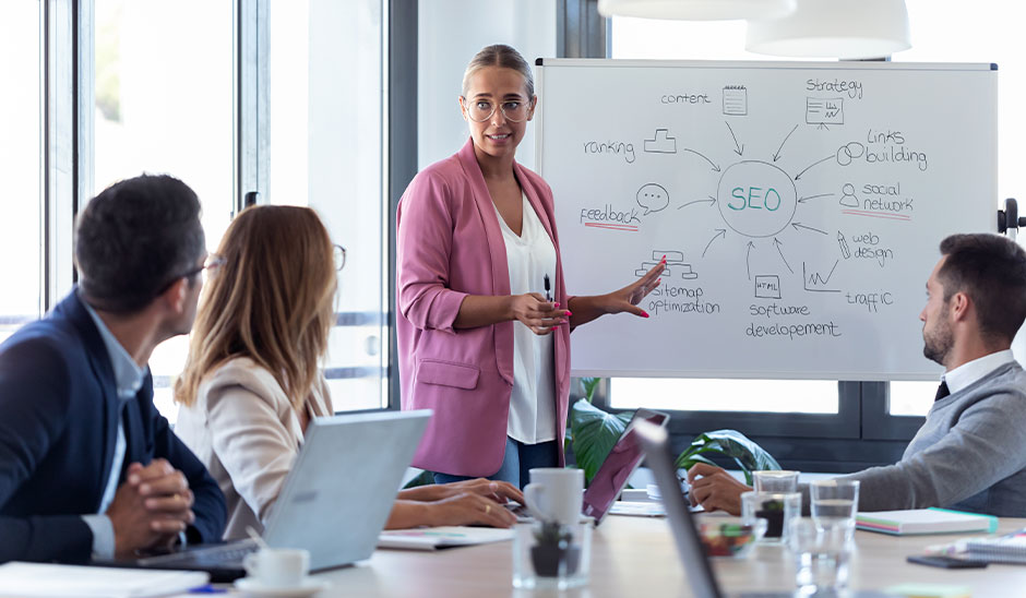A woman presenting SEO concepts on a whiteboard to a meeting audience.