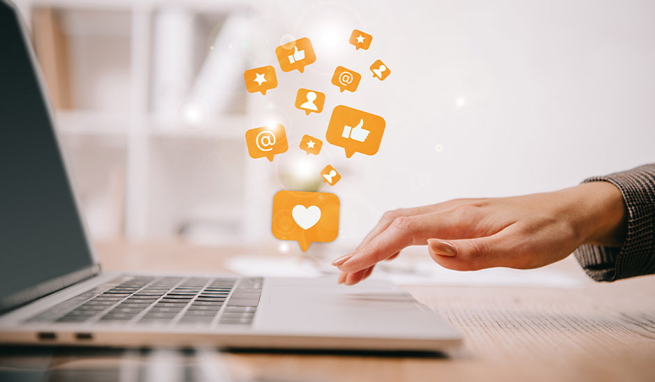 A hand reaching for a laptop keyboard with social media icons floating above.