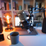 Cozy Podcasting Setup | Idea Stream Marketing Close-up of a microphone on a boom arm, laptop, cup, and speakers in a cozy podcasting setup.