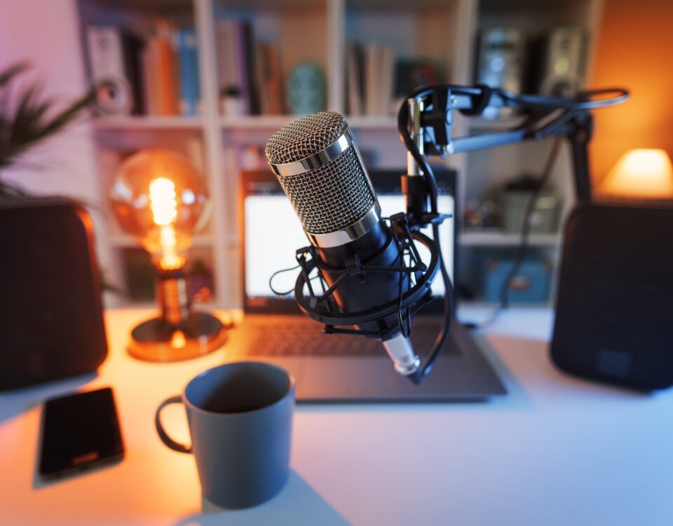 Close-up of a microphone on a boom arm, laptop, cup, and speakers in a cozy podcasting setup.