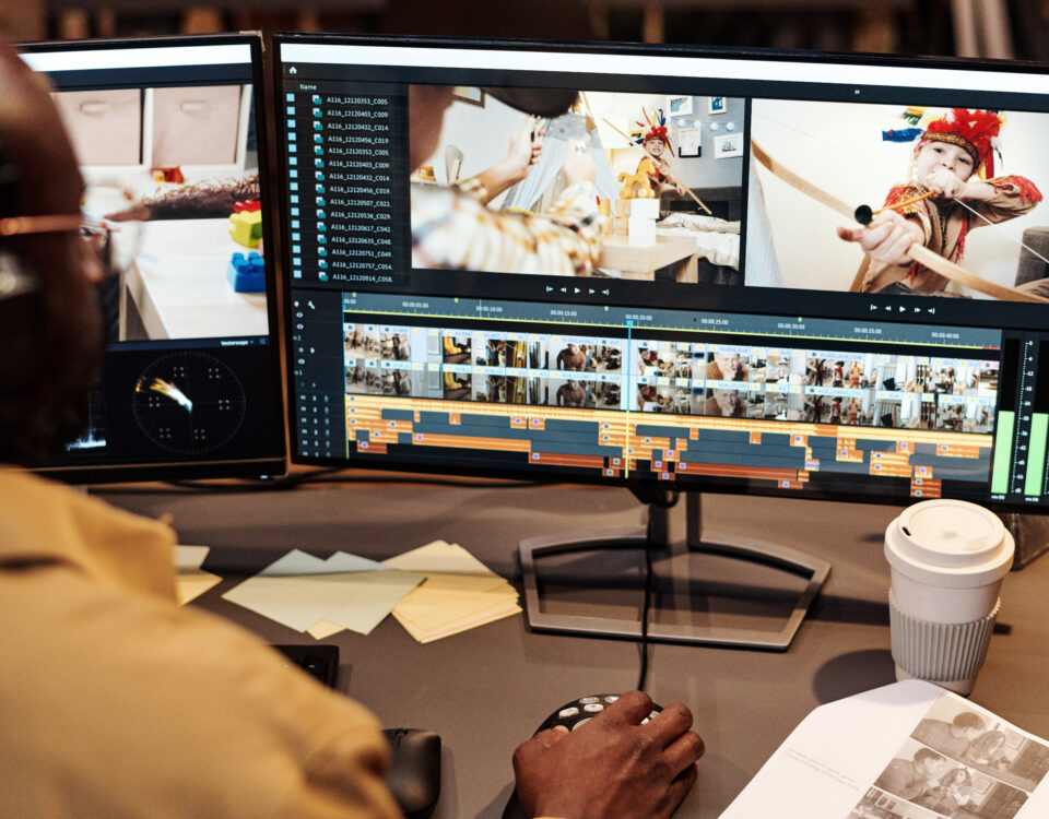 A video editor working on dual monitors, editing clips of children in a playful setting.