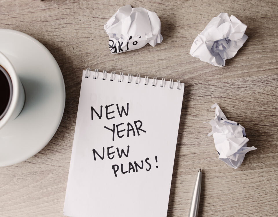 Notebook with the words 'New Year New Plans!' beside a cup of coffee and crumpled paper.