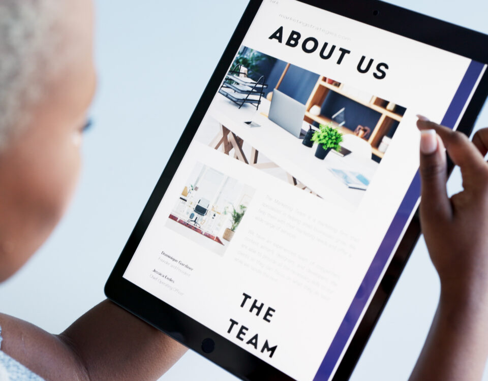 Person interacting with a tablet displaying an 'About Us' webpage design for a marketing agency.