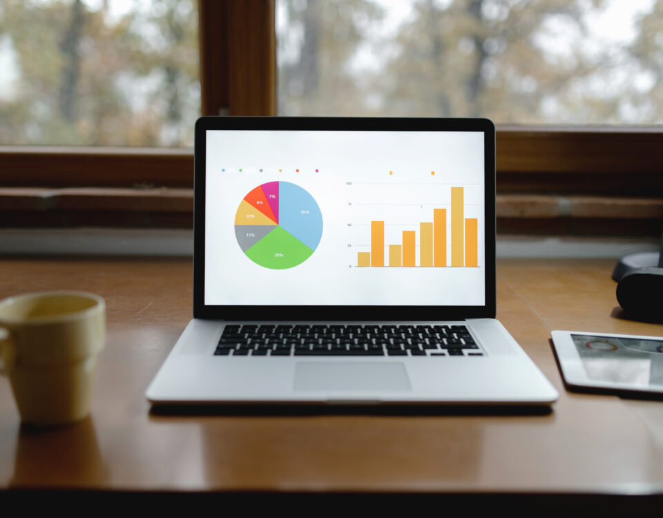 A laptop displaying colorful charts and graphs on a wooden desk, with a coffee cup nearby.