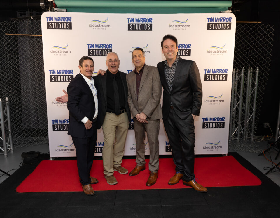 Four men posing on a red carpet in front of a backdrop featuring Tin Mirror Studios and Idea Stream Marketing logos.