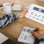 Exploring SEO Concepts on Tablet | Idea Stream Marketing Person using a tablet displaying SEO concepts, with handwritten notes on a notepad.