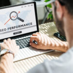 Developer working on laptop displaying SEO performance metrics with a magnifying glass overlay.