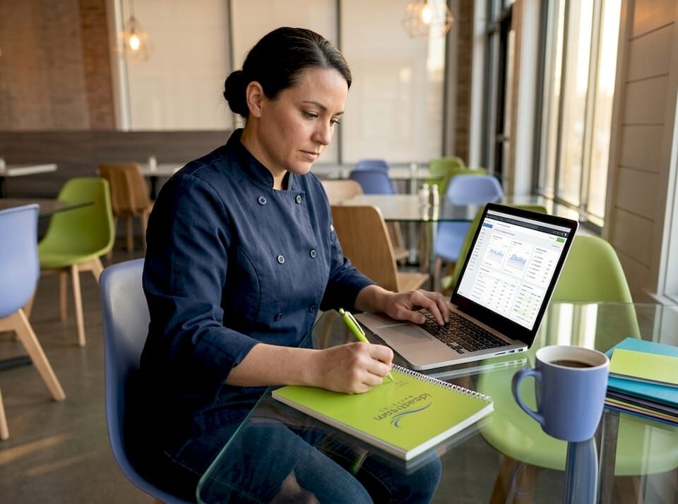 Restaurant owner reviewing marketing analytics on a laptop in a bright café.