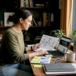 Woman reviewing website development plans with a laptop and notes at a desk.