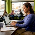 Woman Updating Business Profile in Cafe | Idea Stream Marketing A woman working on a laptop in a cafe, with plants and notes on the table.