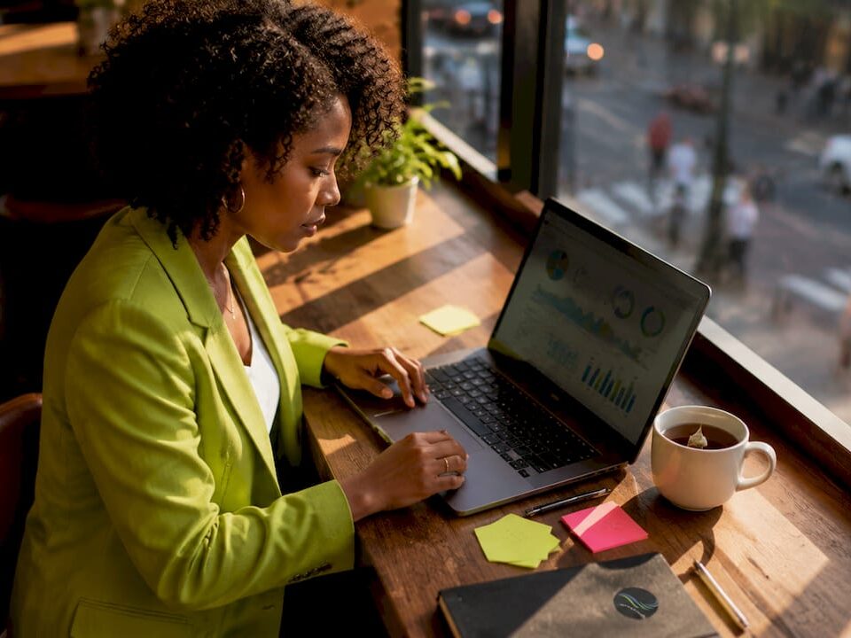 A focused marketer in a bright home office analyzing data on a laptop, with sticky notes and a cup of coffee nearby.