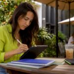 Female social media manager planning workflow using a tablet in an outdoor coworking space.
