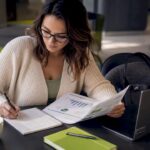 Healthcare Content Strategist at Work | Idea Stream Marketing A woman analyzing a report and taking notes at a desk with a laptop and coffee.