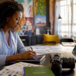 Woman Planning Video Marketing Strategy | Idea Stream Marketing Woman planning video marketing strategy at her desk with a laptop, camera, and tea.