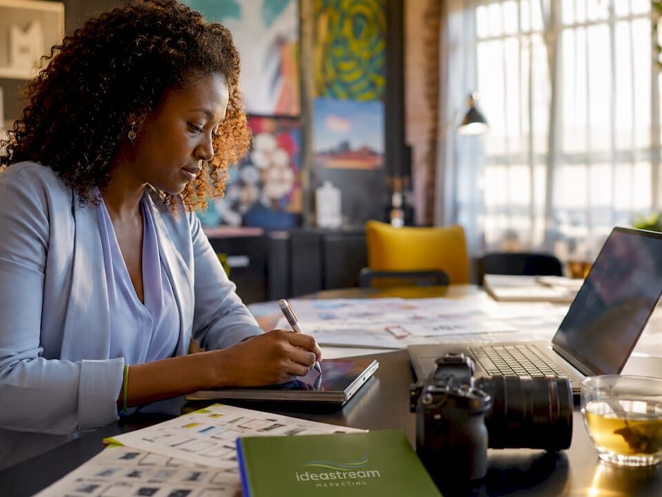 Woman planning video marketing strategy at her desk with a laptop, camera, and tea.