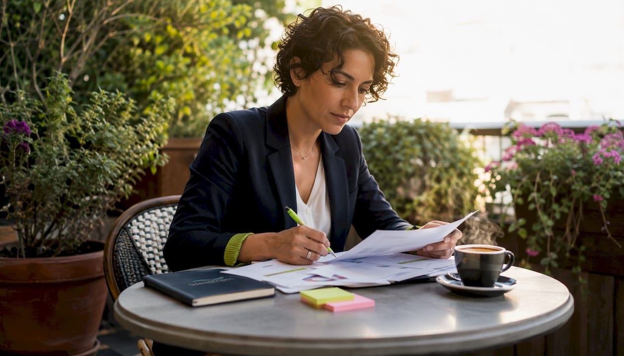A woman reviewing her marketing strategy documents while seated at a table outdoors with coffee.
