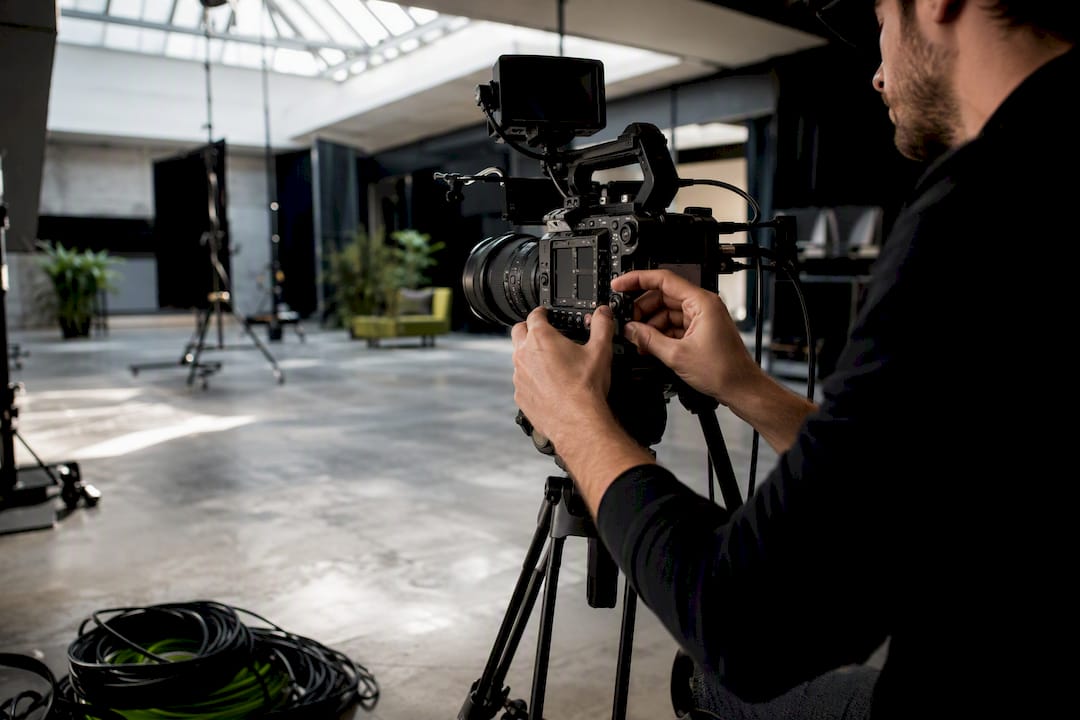 Person adjusting the lens of a professional video camera on a tripod in a well-lit studio.