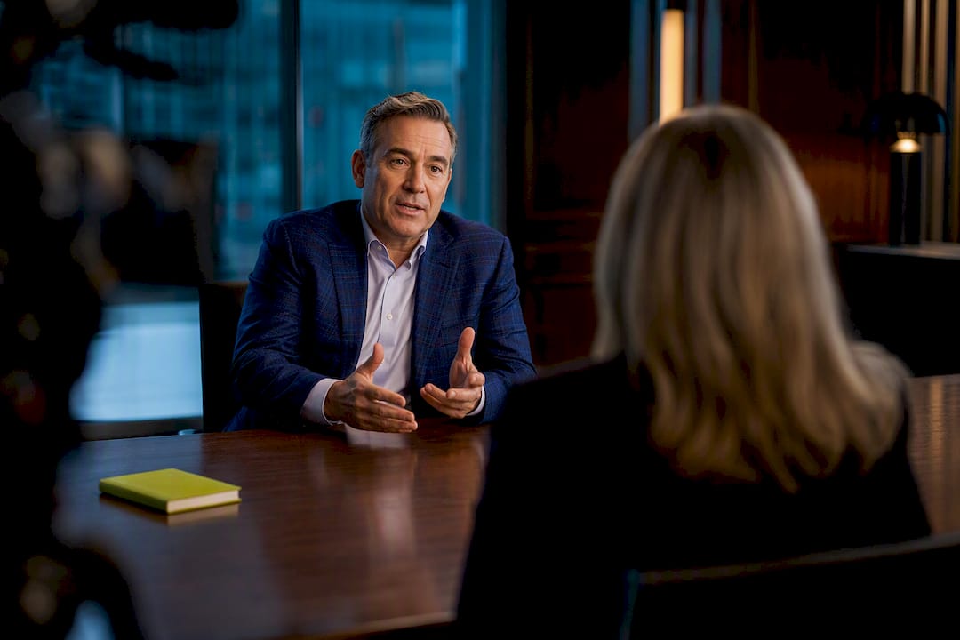 Corporate interview setup with a man discussing at a boardroom table, a notebook visible.