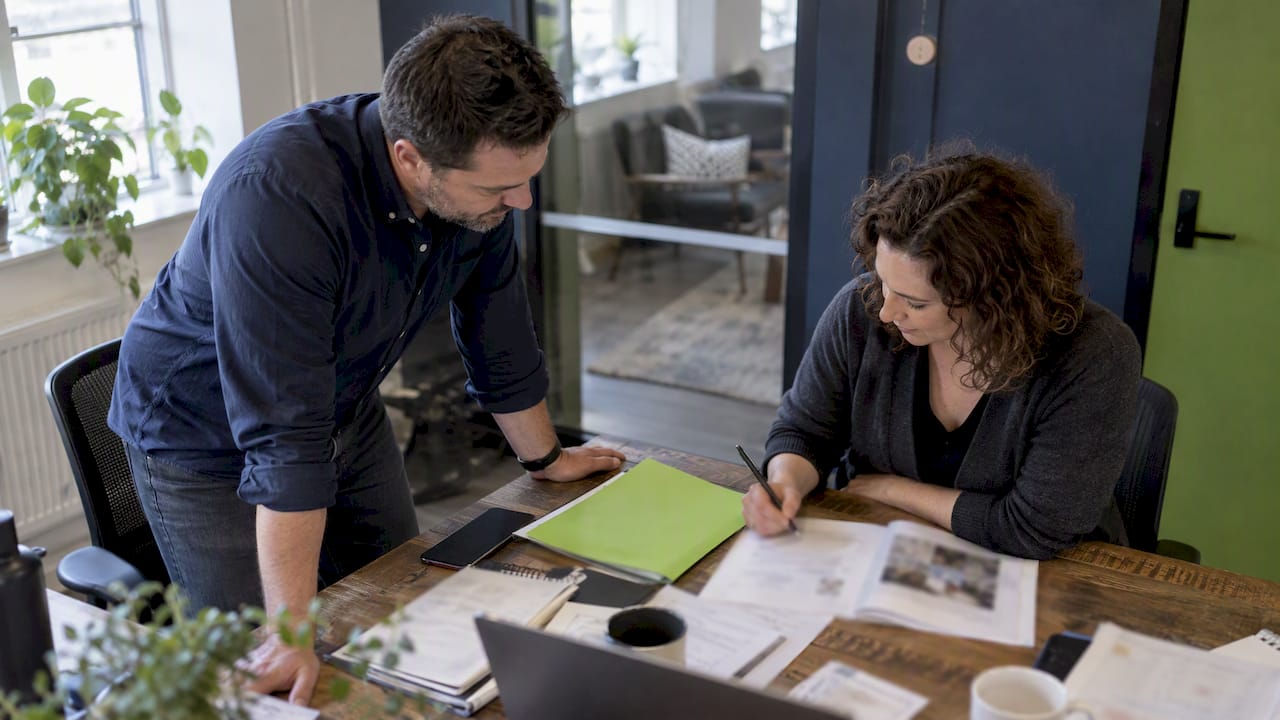 Two professionals collaborating at a desk, reviewing documents and notes in a modern office space.