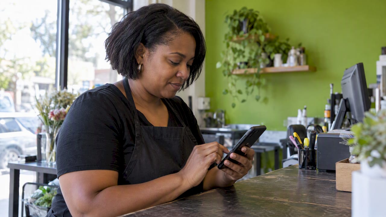 Local business owner checking Google reviews on a smartphone in a cafe.