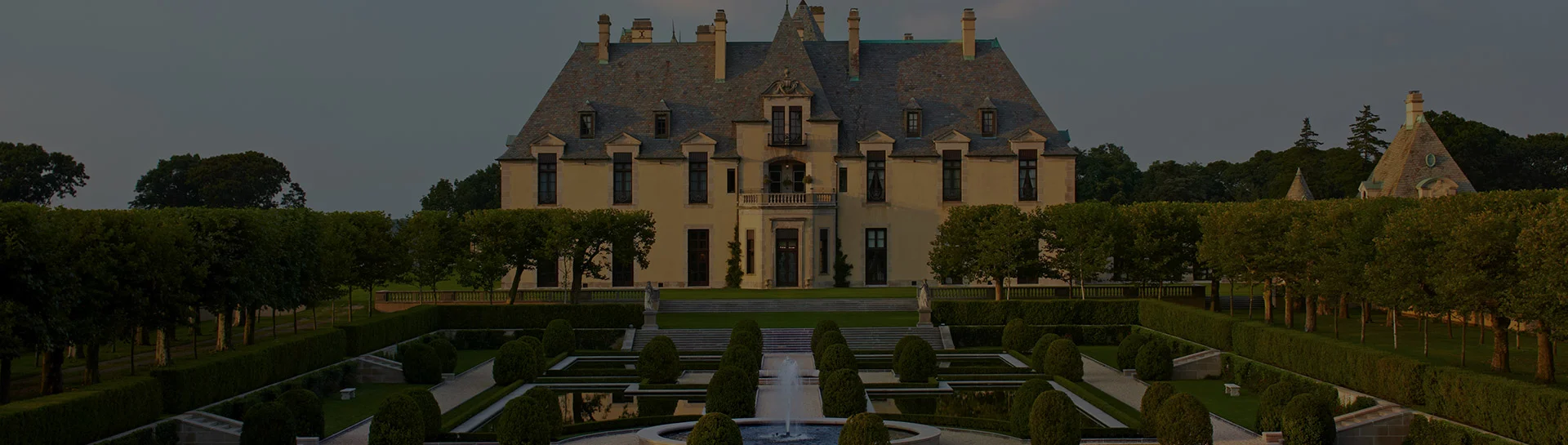 Oheka Castle surrounded by manicured gardens and hedges at dusk.