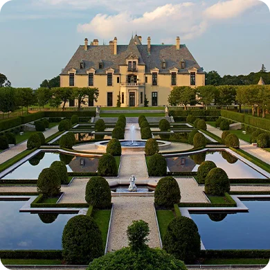 Oheka Castle surrounded by perfectly trimmed hedges and reflective ponds in a manicured garden.