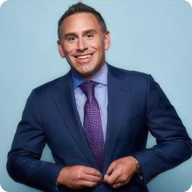 Smiling man in a suit adjusting his jacket, against a light blue background.