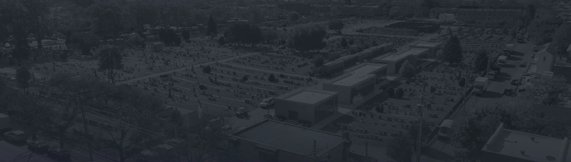 Aerial view of a cemetery with numerous gravestones and surrounding trees.