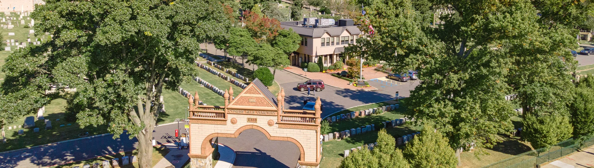 Aerial view of Cypress Hills Cemetery entrance and surrounding landscape with gravestones and trees.