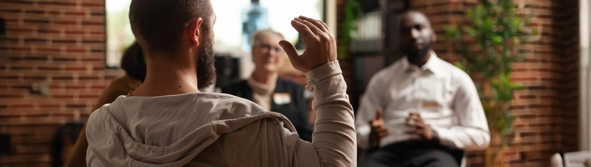 A group discussion in a cozy space with a participant raising their hand to speak.
